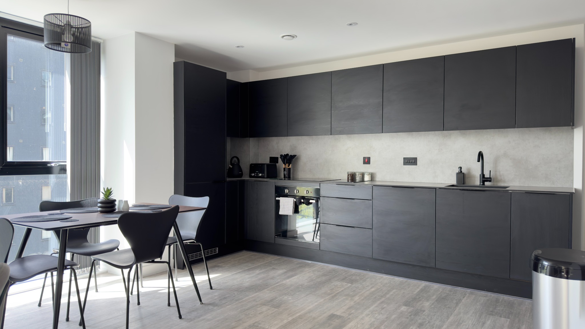 Contemporary apartment kitchen and dining area with charcoal cabinetry and full-height windows